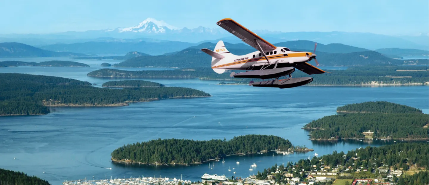Photo of a Kenmore Air plane flying over Friday Harbor with views of the Salish Sea and Mt. Baker
